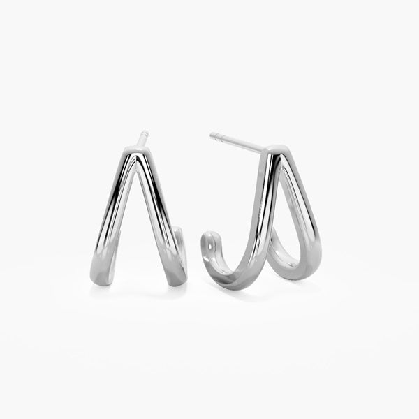 Silver double tapered teardrop pin drop earrings worn on model's ear, shown up close with curly hair and French tip nails in background.