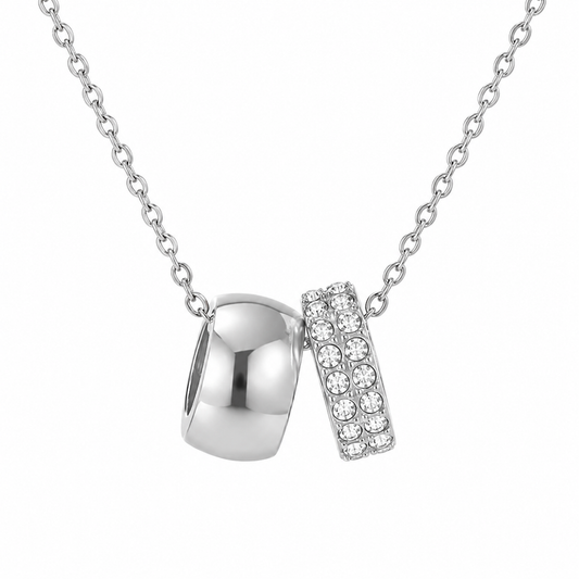Dainty silver chain necklace with polished silver ring and crystal pave band pendant on white background.